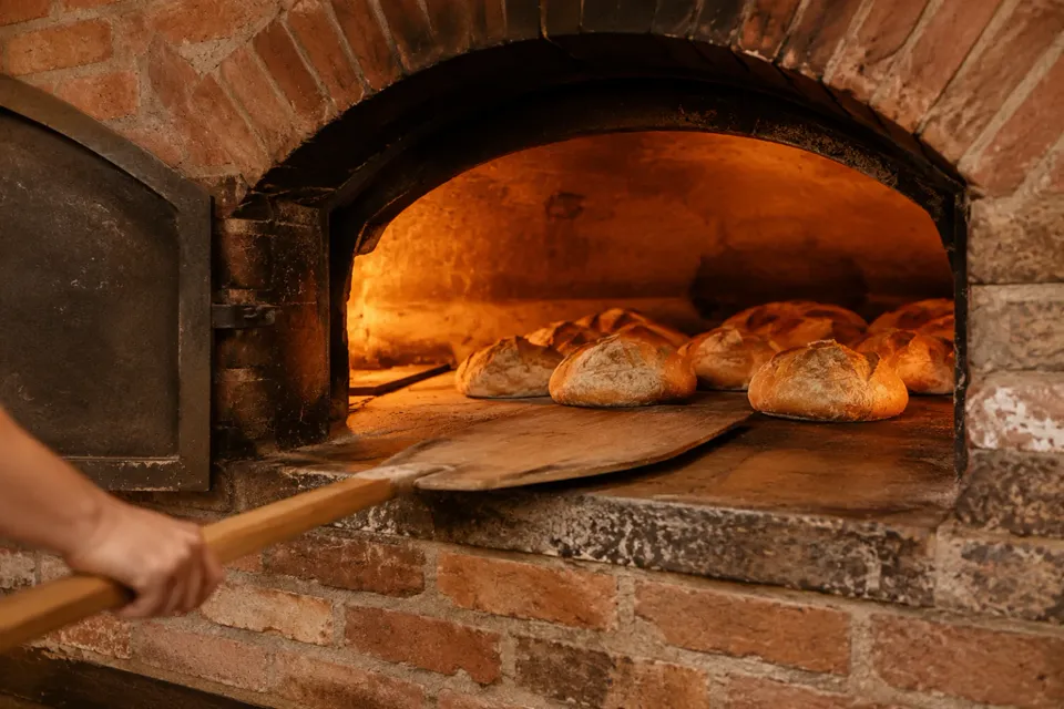 Horno de ladrillo antiguo con panes y una pala de madera